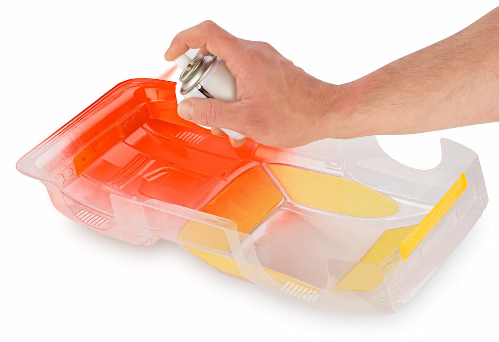 person spray painting a clear RC car body